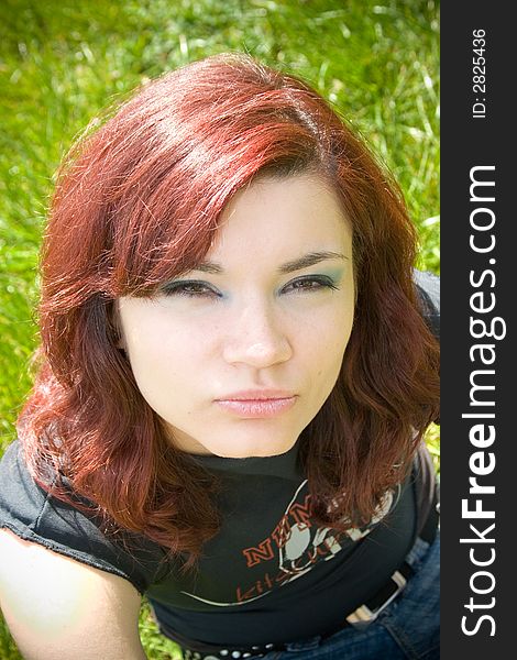 A pretty young woman looks into the camera while sitting on the grass. A pretty young woman looks into the camera while sitting on the grass.