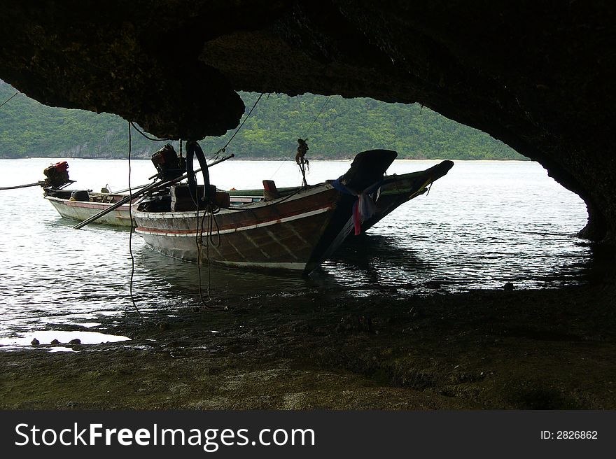 Two thai long boats moored on an island next to a large rock. Two thai long boats moored on an island next to a large rock