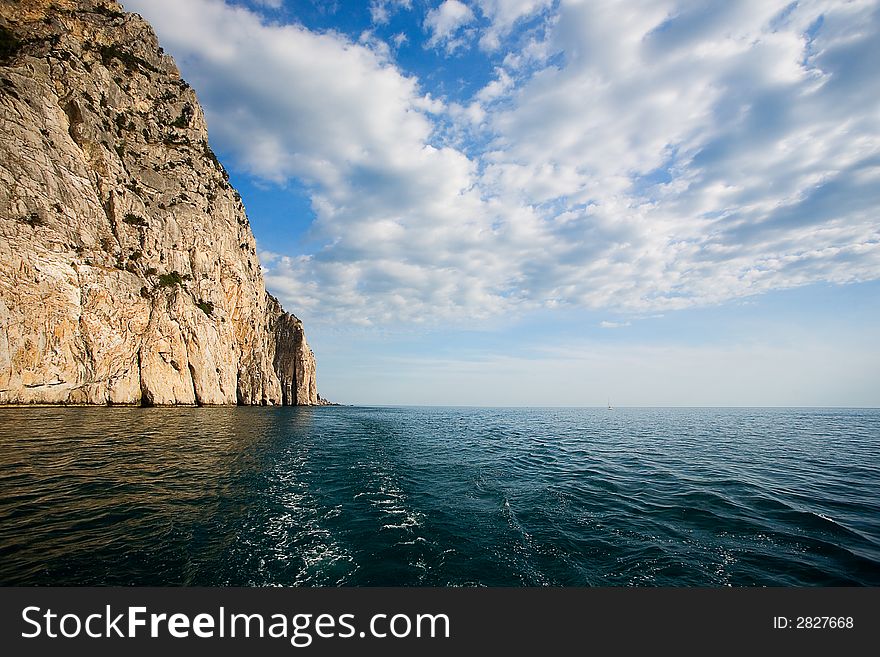 After-tossing of the ship floating across Black sea. The steep rock and the cloudy sky is seen. After-tossing of the ship floating across Black sea. The steep rock and the cloudy sky is seen