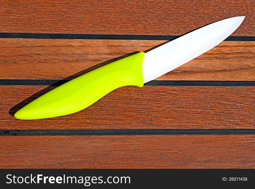 A ceramic knife with a white blade and a green grip on a wooden cutting board. A ceramic knife with a white blade and a green grip on a wooden cutting board.