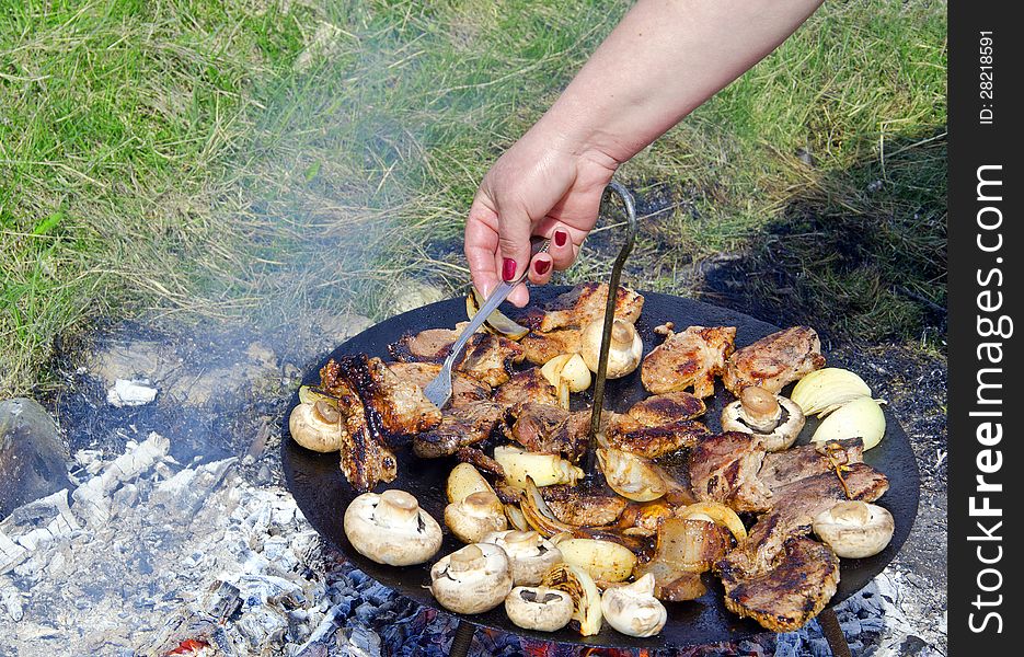 Woman hand with a pitchfork making a barbecue with meat, ham, onion and mushrooms. Woman hand with a pitchfork making a barbecue with meat, ham, onion and mushrooms