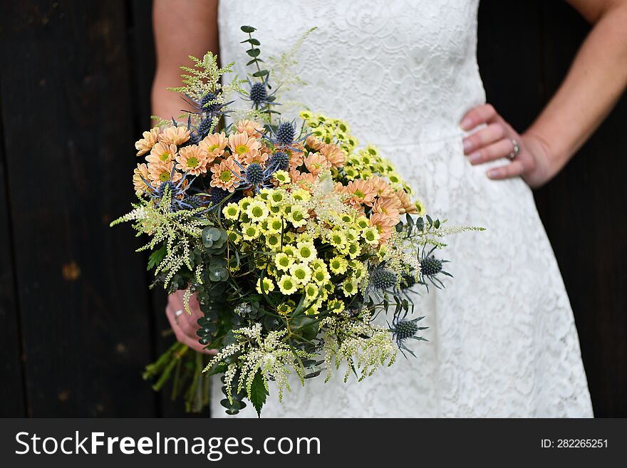 the bride holds a large bouquet of yellow and orange meadow flowers with eucalyptus