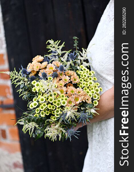 the bride in a white dress holds a large bouquet of yellow and orange meadow flowers with eucalyptus