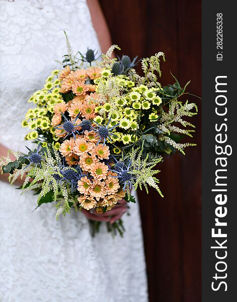 the bride holds a large bouquet of yellow and orange meadow flowers with eucalyptus