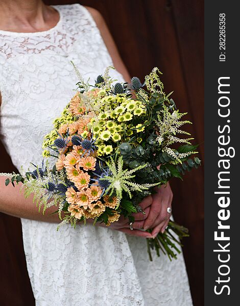 the bride holds a large bouquet of yellow and orange meadow flowers with eucalyptus