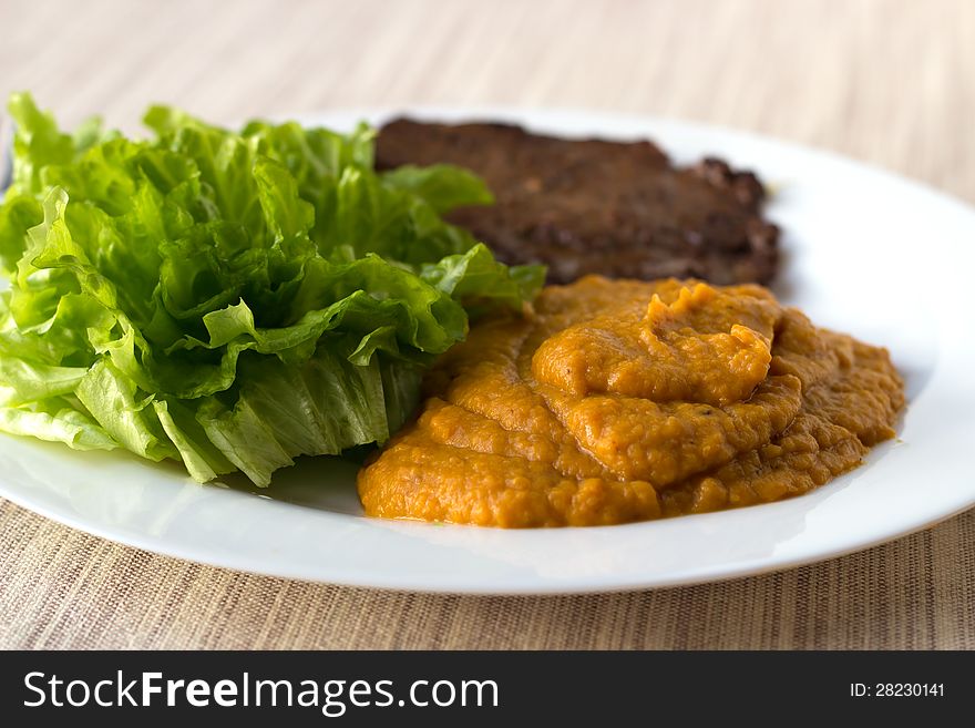 Chestnut-carrot-pumpkin mashed mix with green salad and a beef steak on the white plate