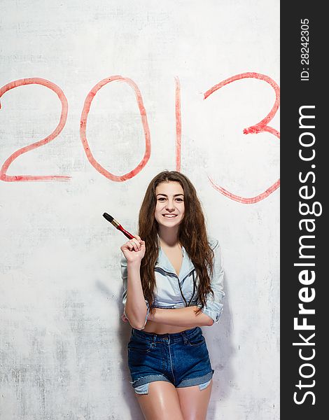 Girl in jeans shorts and jacket draws a Christmas (new year) decoration on old white wall with the red paint. Girl in jeans shorts and jacket draws a Christmas (new year) decoration on old white wall with the red paint.