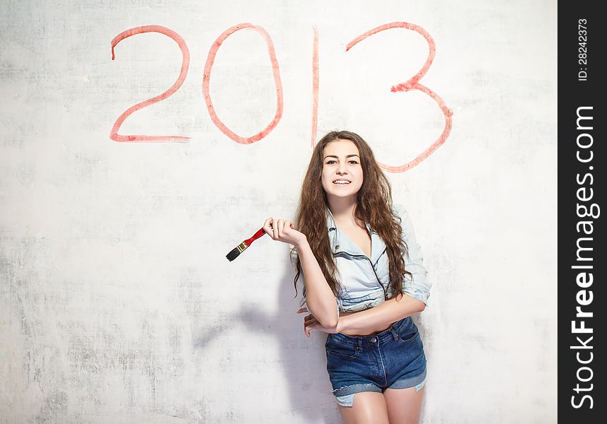 Girl in jeans shorts and jacket draws a Christmas (new year) decoration on old white wall with the red paint. Girl in jeans shorts and jacket draws a Christmas (new year) decoration on old white wall with the red paint.