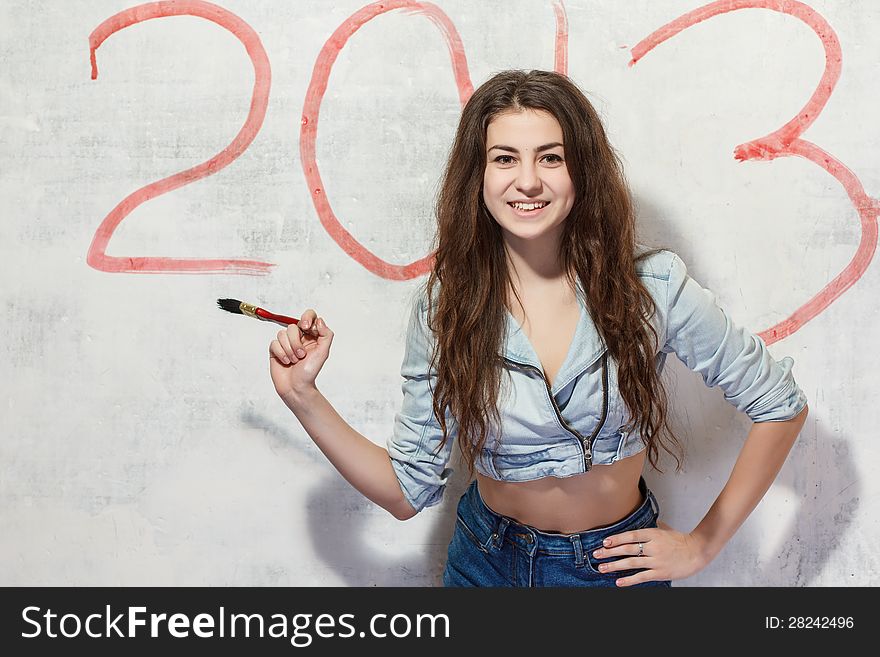 Girl in jeans shorts and jacket draws a Christmas (new year) decoration on old white wall with the red paint. Girl in jeans shorts and jacket draws a Christmas (new year) decoration on old white wall with the red paint.