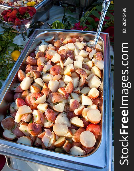 A serving dish of cooked potatoes and a serving spoon in the buffet line of a wedding reception. The meal looks healthy and delicious. A serving dish of cooked potatoes and a serving spoon in the buffet line of a wedding reception. The meal looks healthy and delicious.