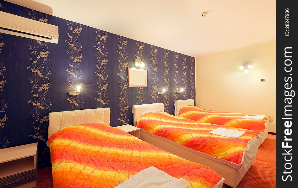 Interior of a hotel room for three persons, blue wallpapers and orange sheets on beds. Interior of a hotel room for three persons, blue wallpapers and orange sheets on beds.