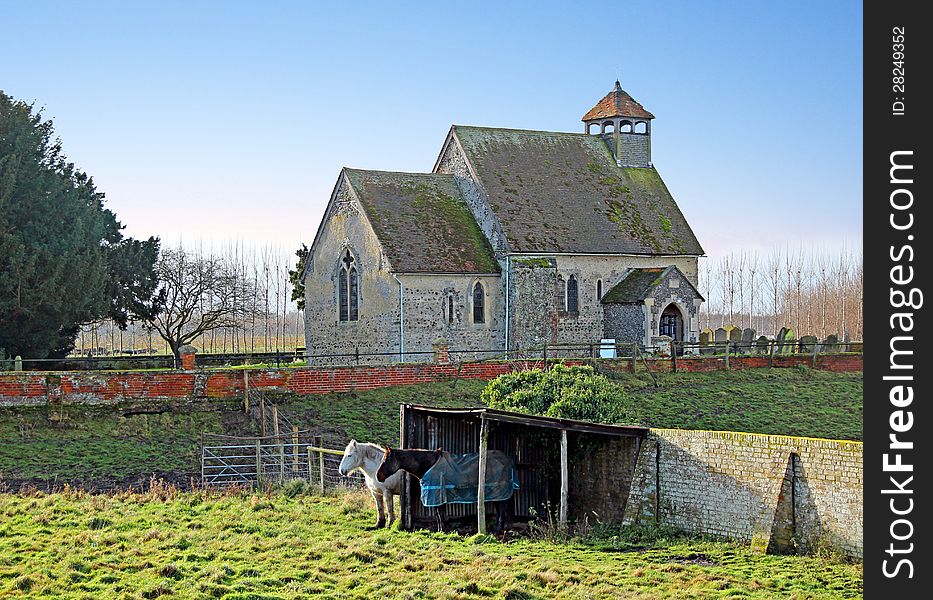 Photo of an ancient saxon church located in goodnestone,graveney in the rural county of kent with horses grazing in the field by their shelter. Photo of an ancient saxon church located in goodnestone,graveney in the rural county of kent with horses grazing in the field by their shelter.