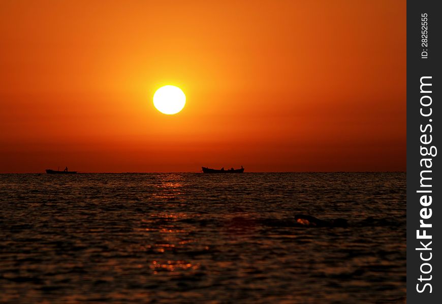 Fishing boat shapes on the horizon line and a man swimming towards them. Fishing boat shapes on the horizon line and a man swimming towards them