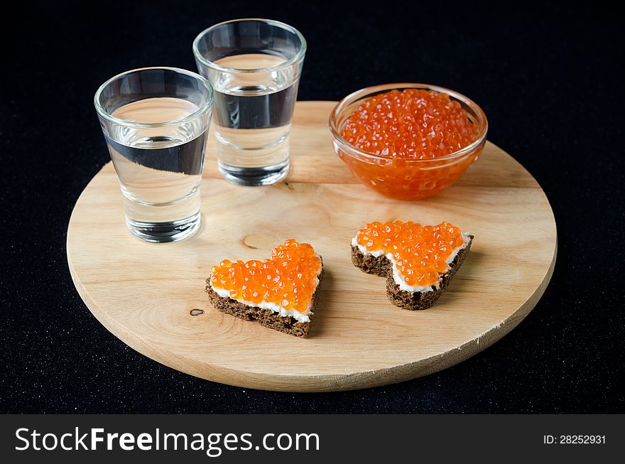 Two sandwich with red caviar in the form of a heart and vodka on a wooden board. Two sandwich with red caviar in the form of a heart and vodka on a wooden board