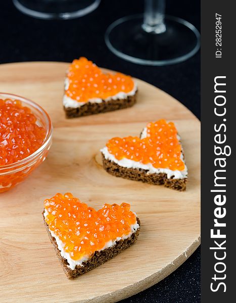 Three sandwich with red caviar in the form of a heart on a wooden board