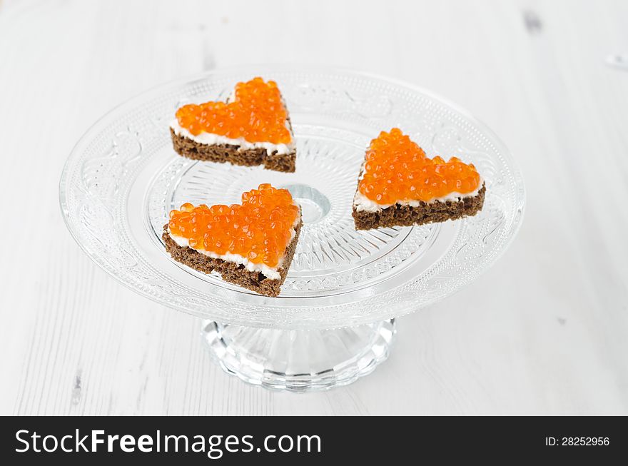 Three sandwich with red caviar in the form of a heart on glass stand base, horizontal