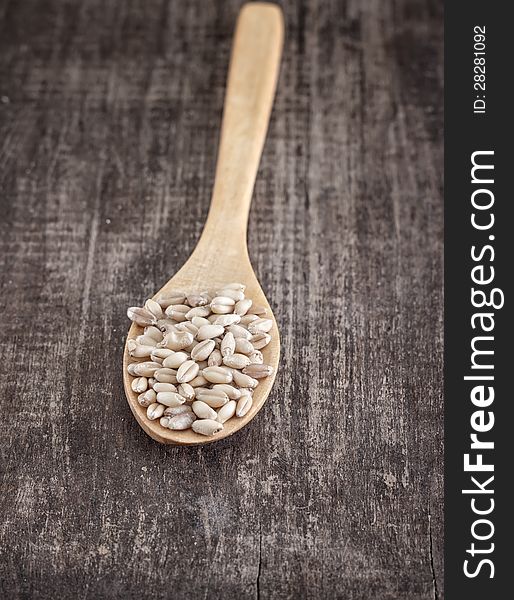 Wheat grain in the wooden spoon over old table