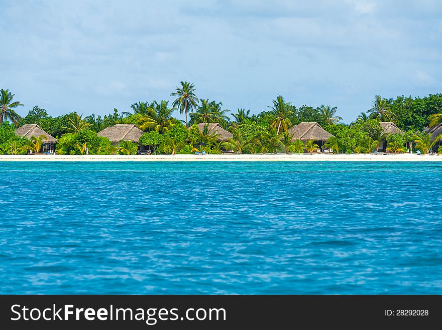 Tropical island hotel beautiful landscape with blue water, green trees, traditional bungalow and cloudy sky