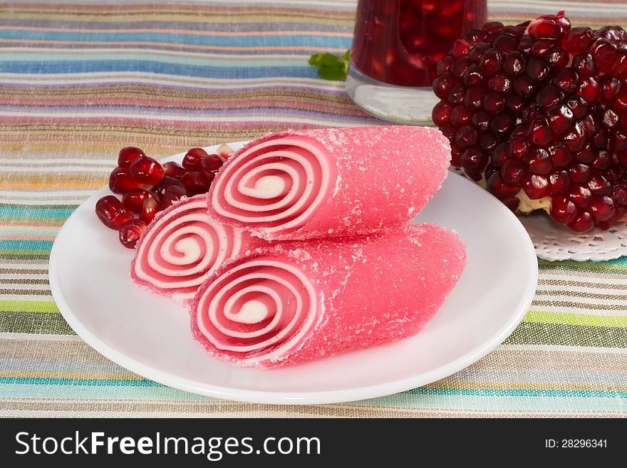 Red candy fruit on a plate with pomegranate, closeup