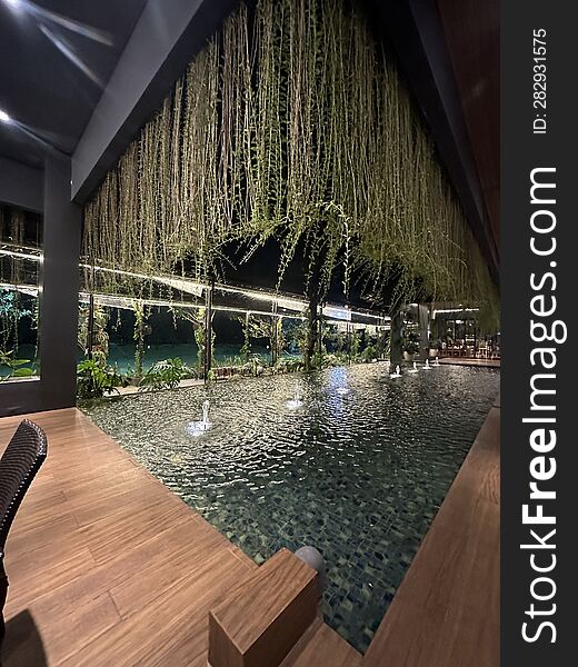 A swimming pool with small water fountains, located indoors in a restaurant in Bintaro, Indonesia. Above it, there are trailing vines adding to the beauty of the ambiance.