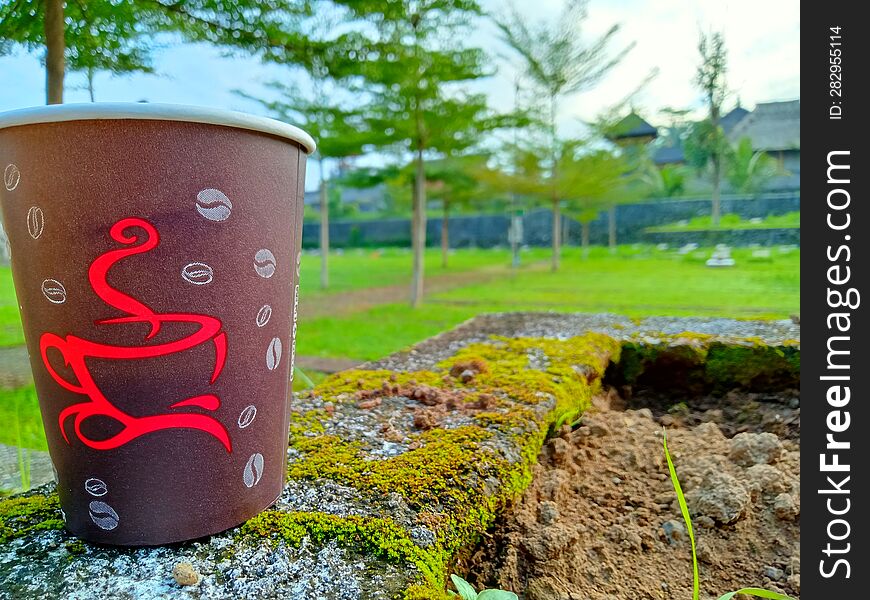 Close Up Photo Of A Paper Cup Filled With Coffee Against A City Park Background In The Morning