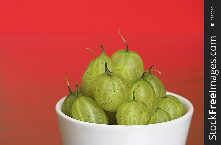 A white bowl filled with fresh gooseberries. On a red background. A white bowl filled with fresh gooseberries. On a red background.
