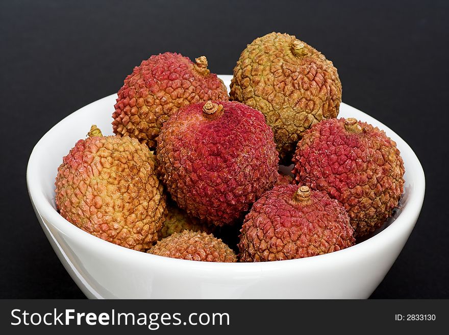 A white bowl filled with fresh lychees - on a black background.