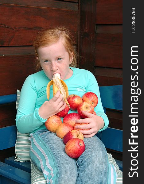 Girl eating banana and holding apples