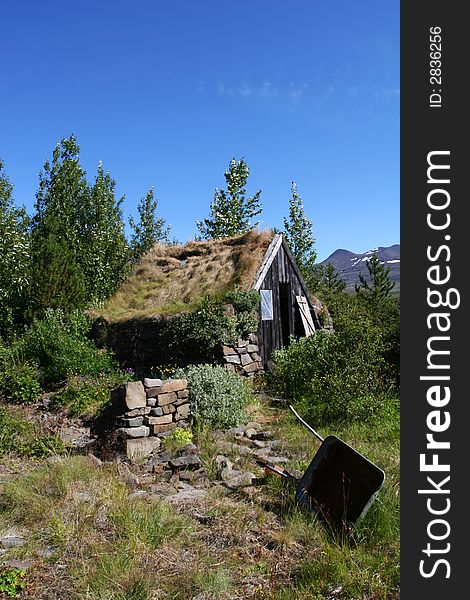 A mountain cabin in disrepair surrounded by growth and trees, mountaintops in the distance. A mountain cabin in disrepair surrounded by growth and trees, mountaintops in the distance