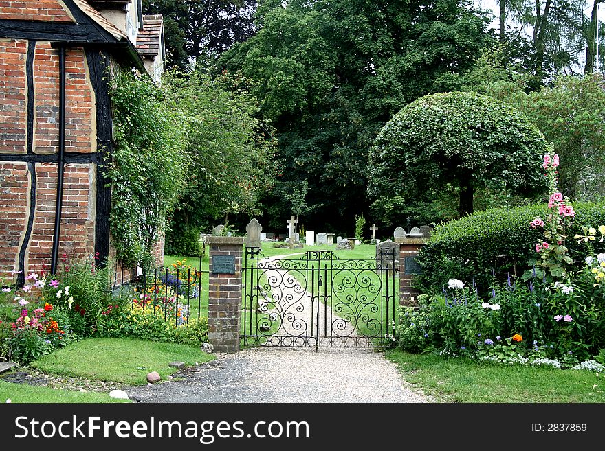 Wrought Iron Entrance Gate to an English Village Churchyard with flowers and Timber Framed Cottage. Wrought Iron Entrance Gate to an English Village Churchyard with flowers and Timber Framed Cottage