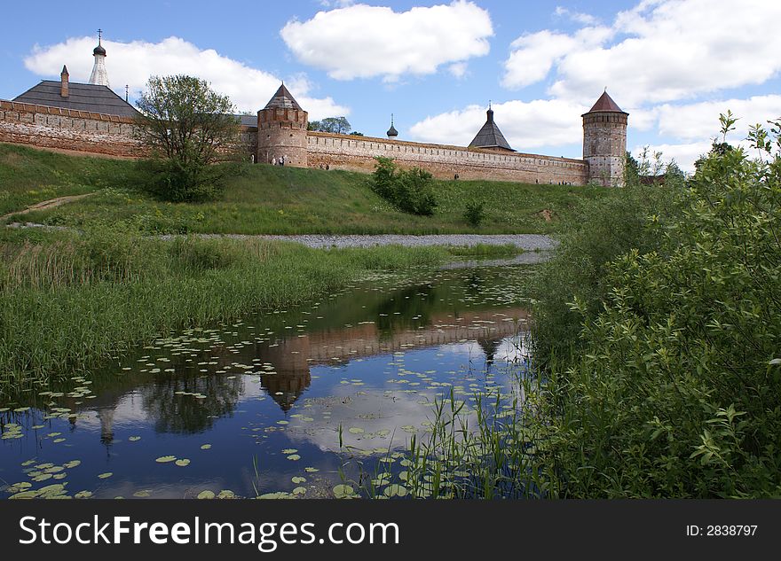 Long red wall and towers of old Russian fort-monastery by the river. Summer. Long red wall and towers of old Russian fort-monastery by the river. Summer
