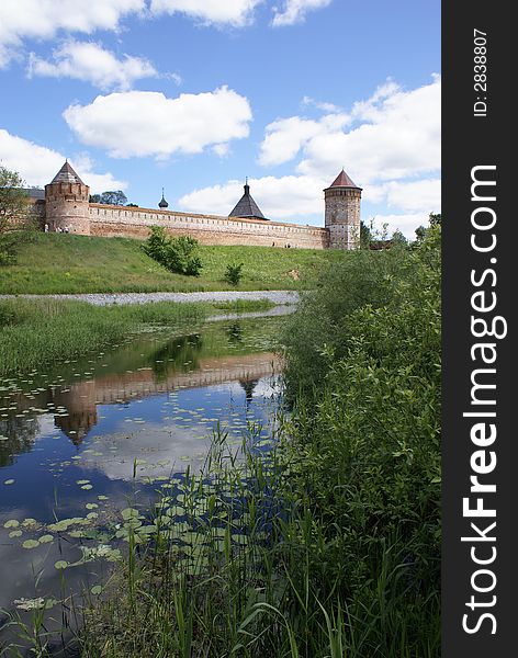 Long red wall and towers of old Russian fort-monastery by the river. Summer. Long red wall and towers of old Russian fort-monastery by the river. Summer