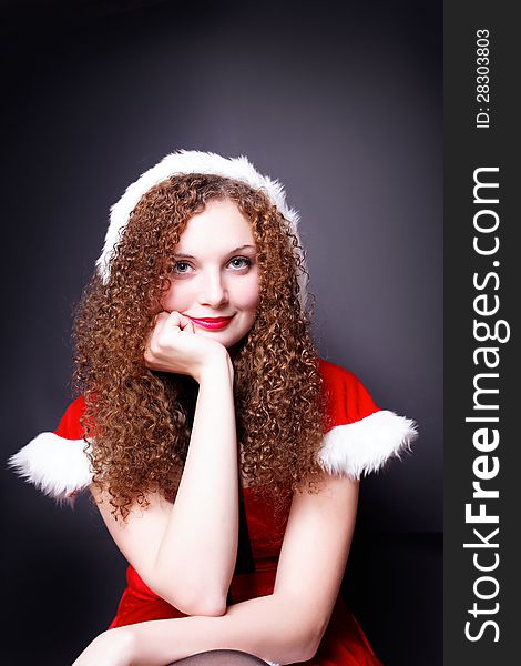 Portrait of pretty curly girl in Santa costume dark background