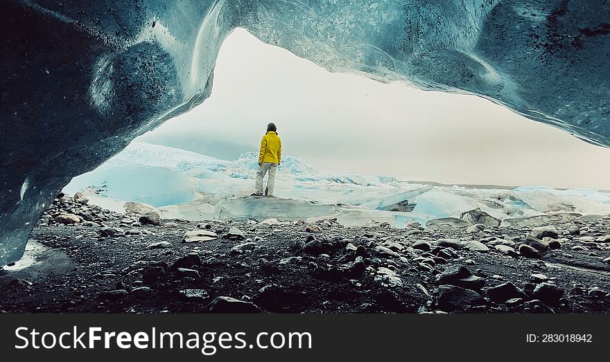 Tourist traveler woman travel in Iceland stand by beautiful FjallsjÃ¶kull glacier in Iceland in overcast day. Cinematic panorama from small gap ice cave