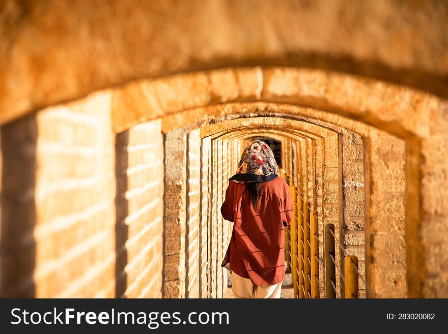 Isfahan, Iran - May 2022: back view woman walk on Sio Se Pol or Bridge of 33 arches, one of the oldest bridges of Esfahan and longest bridge on Zayandeh River