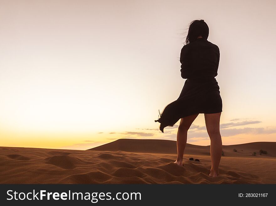 Woman stand enjoy sand dunes in desert watch sunset relax on golden hour alone. Travel lifestyle and wellness concept. Cinematic wanderlust background