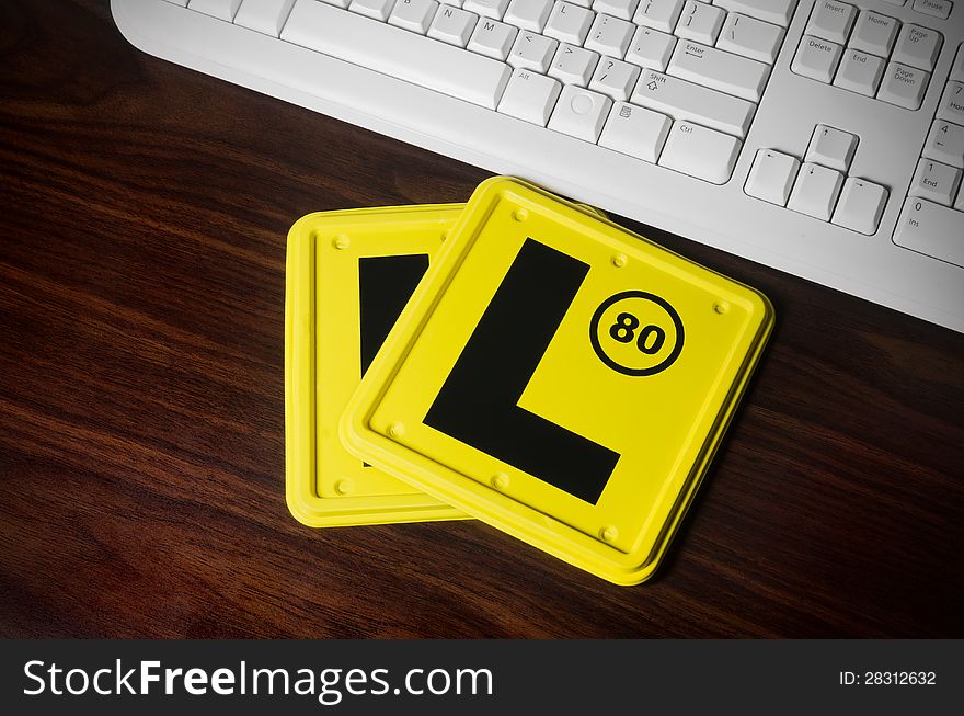 Two L plates laying on the computer desk next to the white keyboard.