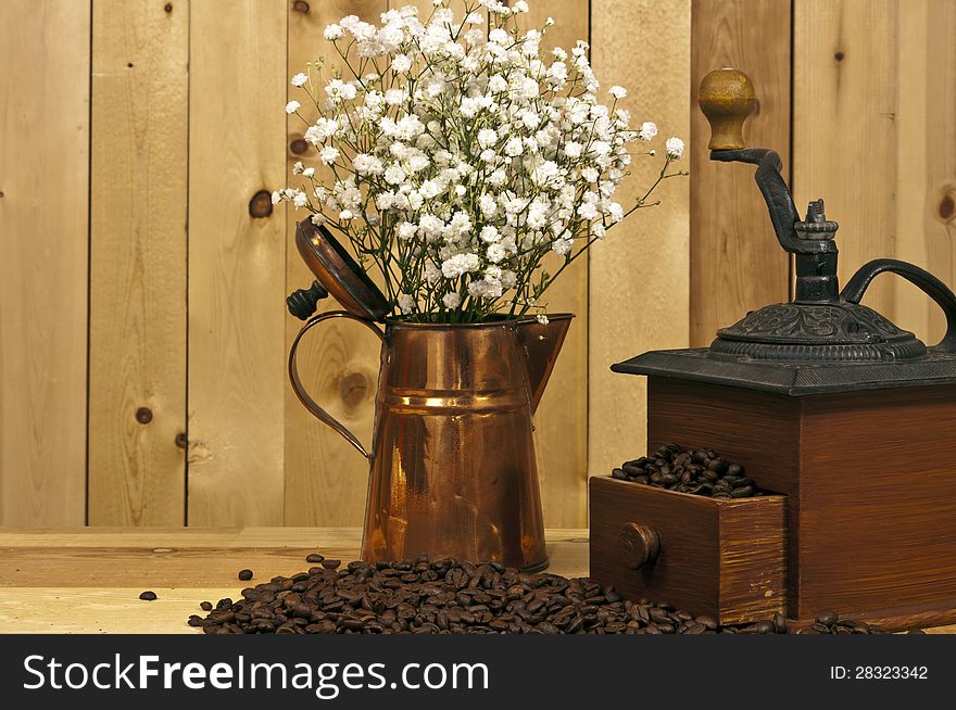 Antique coffee grinder and beans with copper picher and flowers on wood background