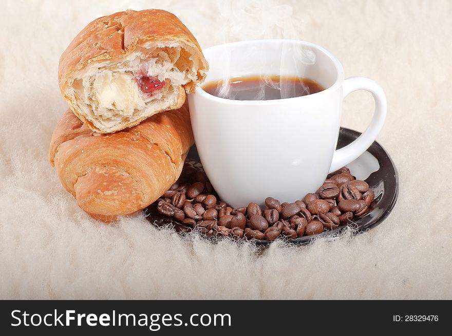 Croissant with coffee and beans on fur background.