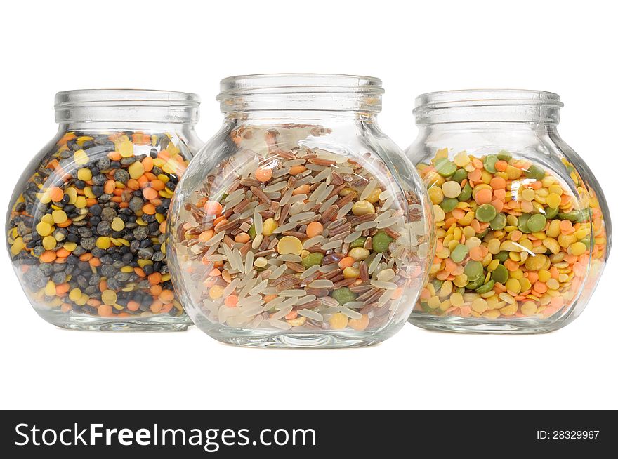 Three glass jars with assorted cereals (lentils, red and parboiled rice, split peas) isolated on a white background - horizontal orientation. Three glass jars with assorted cereals (lentils, red and parboiled rice, split peas) isolated on a white background - horizontal orientation