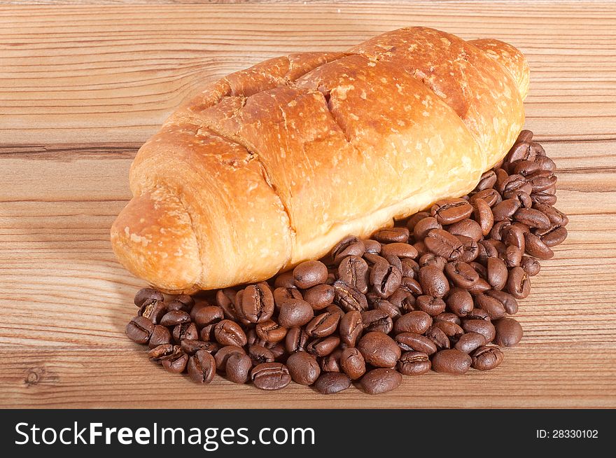 Croissant with coffee beans on wooden background.