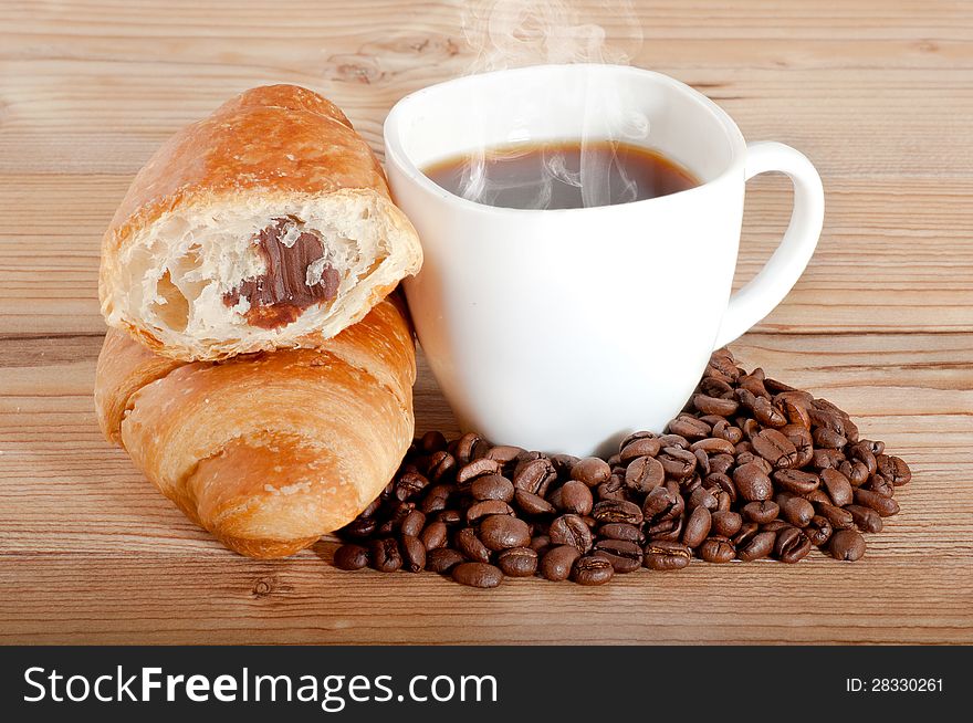 Croissant with coffee and beans on wooden background.