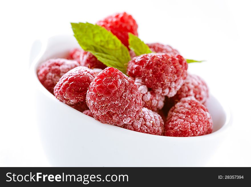 Bowl of refreshing frozen raspberries covered in frosting for a delicious healthy dessert, tilted closeup angle. Bowl of refreshing frozen raspberries covered in frosting for a delicious healthy dessert, tilted closeup angle