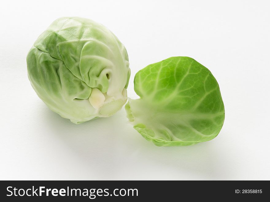 Head or bud of a fresh green brussel sprout, brassica oleracea, with a single loose leaf on a white studio background. Head or bud of a fresh green brussel sprout, brassica oleracea, with a single loose leaf on a white studio background