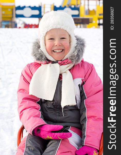 Beautiful smiling little girl sitting on a sled in snow laughing at the camera as she enjoys the freedom of a winter playground. Beautiful smiling little girl sitting on a sled in snow laughing at the camera as she enjoys the freedom of a winter playground