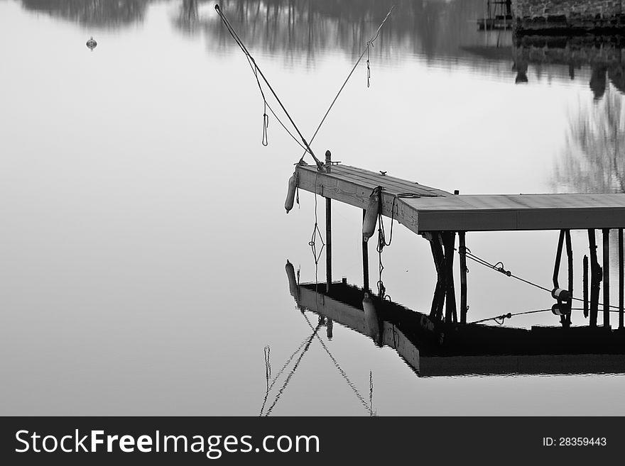 Fishing poles sitting on a dock over a still lake in black & white with a reflection in the water. Fishing poles sitting on a dock over a still lake in black & white with a reflection in the water