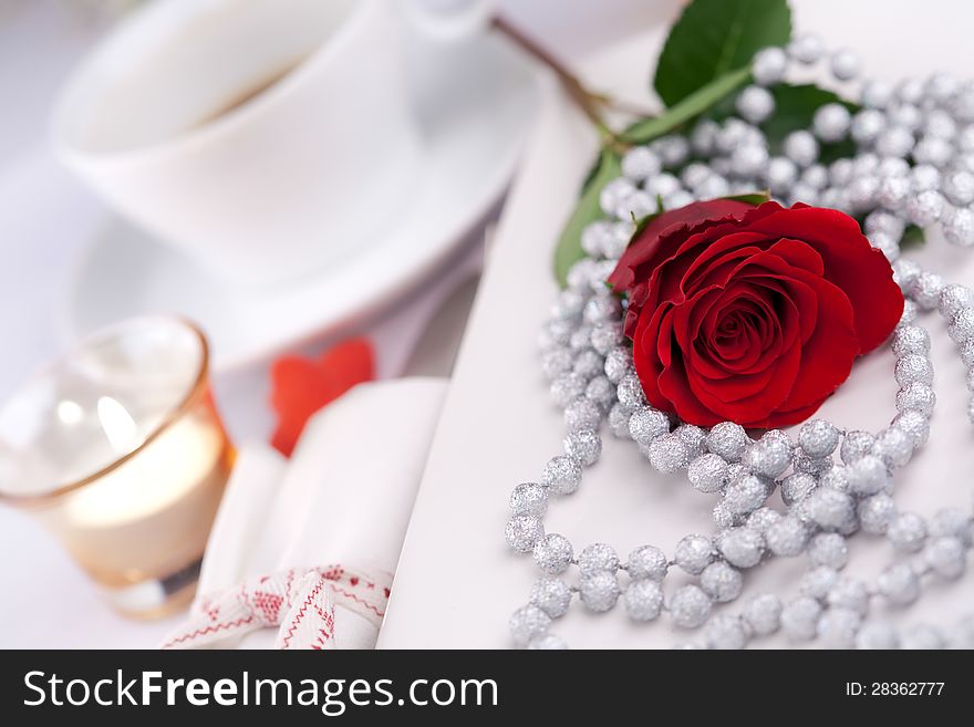 Romantic table setting with a single red rose, decorative necklace and candle to celebrate Valentines day, anniversary, wedding or engagement