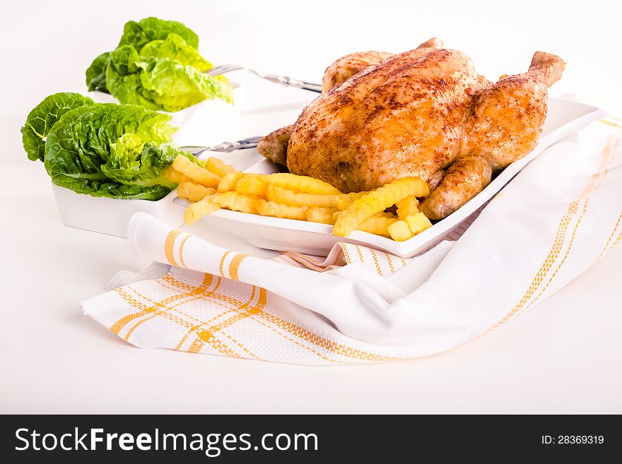 Crisp golden roast chicken served with side dishes of fresh fried crinkly French fries and ripe red tomatoes for a delicious meal