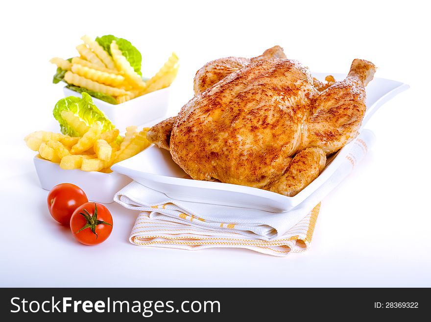 Crisp golden roast chicken served with side dishes of fresh fried crinkly French fries and ripe red tomatoes for a delicious meal