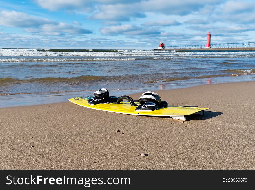 A yellow kiteboard on a Lake Michigan beach with red lighthouse in the background. A yellow kiteboard on a Lake Michigan beach with red lighthouse in the background